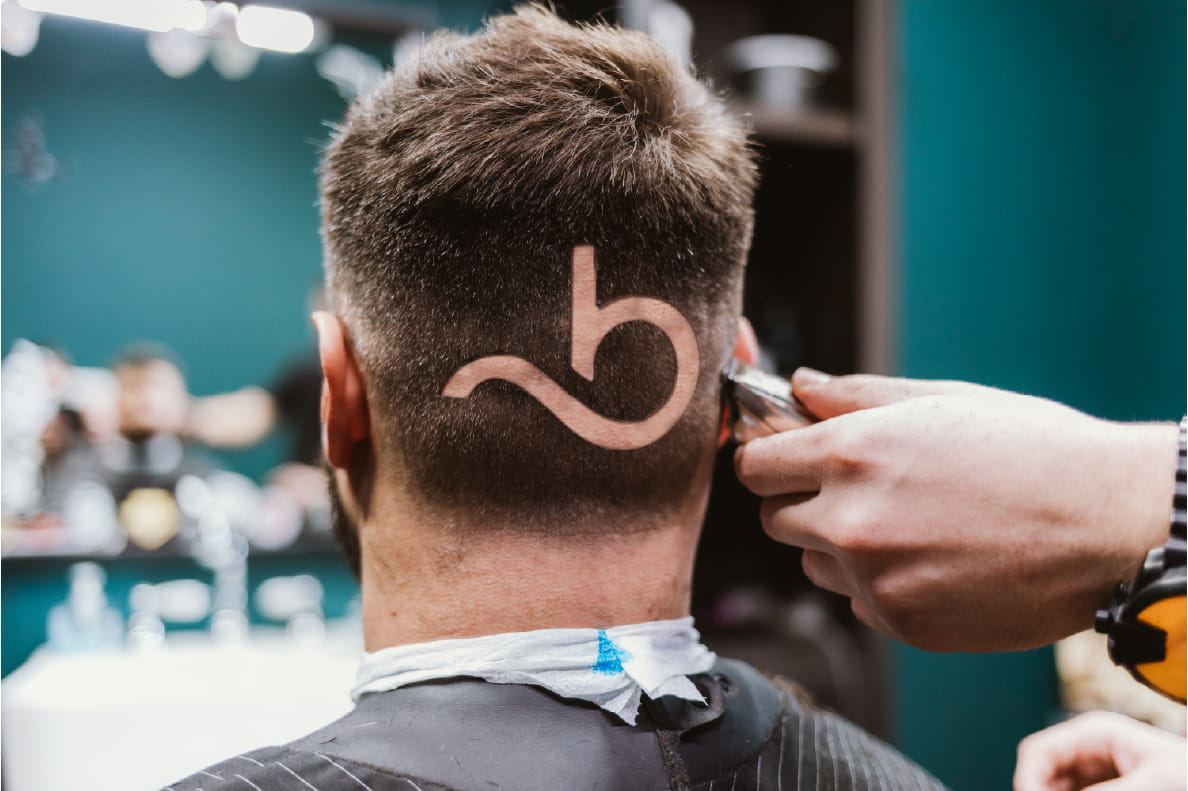 A barbershop scene, tightly cropped on the back of a mans head where the booksy logo has been shaved into his hair.